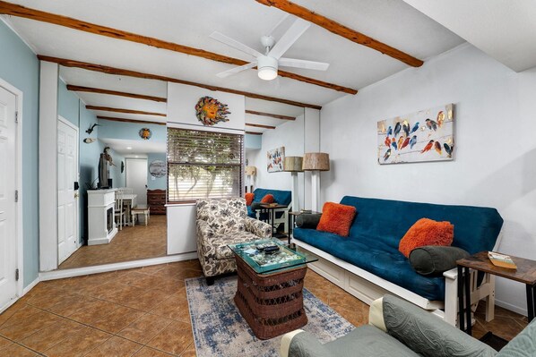 A living room with a blue sofa, a patterned armchair, a glass coffee table, and a ceiling fan.