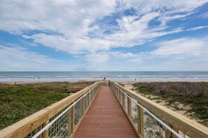 Une promenade en bois qui mène à une plage, avec un ciel dégagé.
