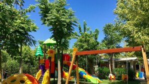 Ein Spielplatz mit Rutschen, Schaukeln und Klettergerüsten, umgeben von Bäumen.