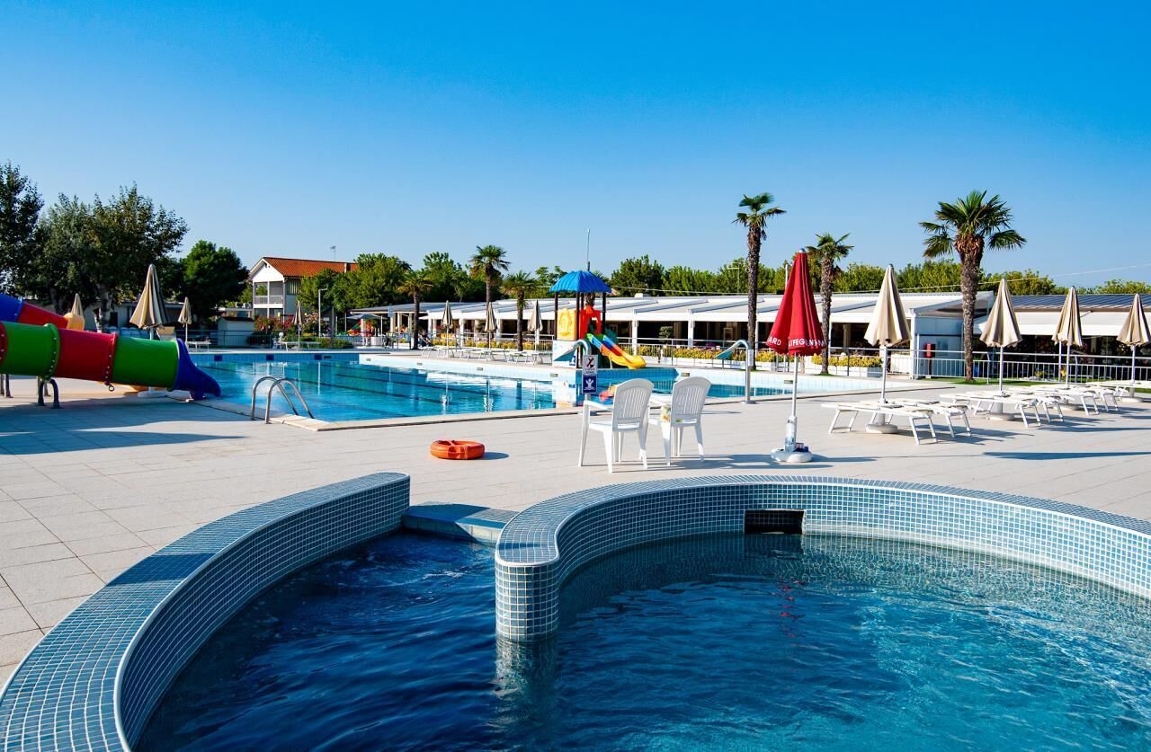 Area piscina con idromassaggio, sedie a sdraio e scivolo acquatico.
