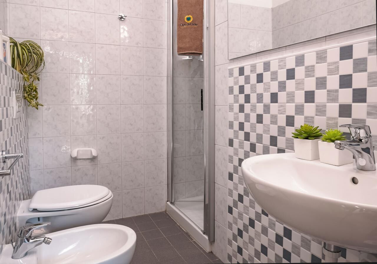 Casa de banho com sanita, bidé e lavatório, com azulejos xadrez e cabine de duche em vidro.