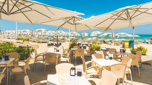 Ein Restaurant direkt am Strand mit Außenbereich, Sonnenschirmen und Meerblick.