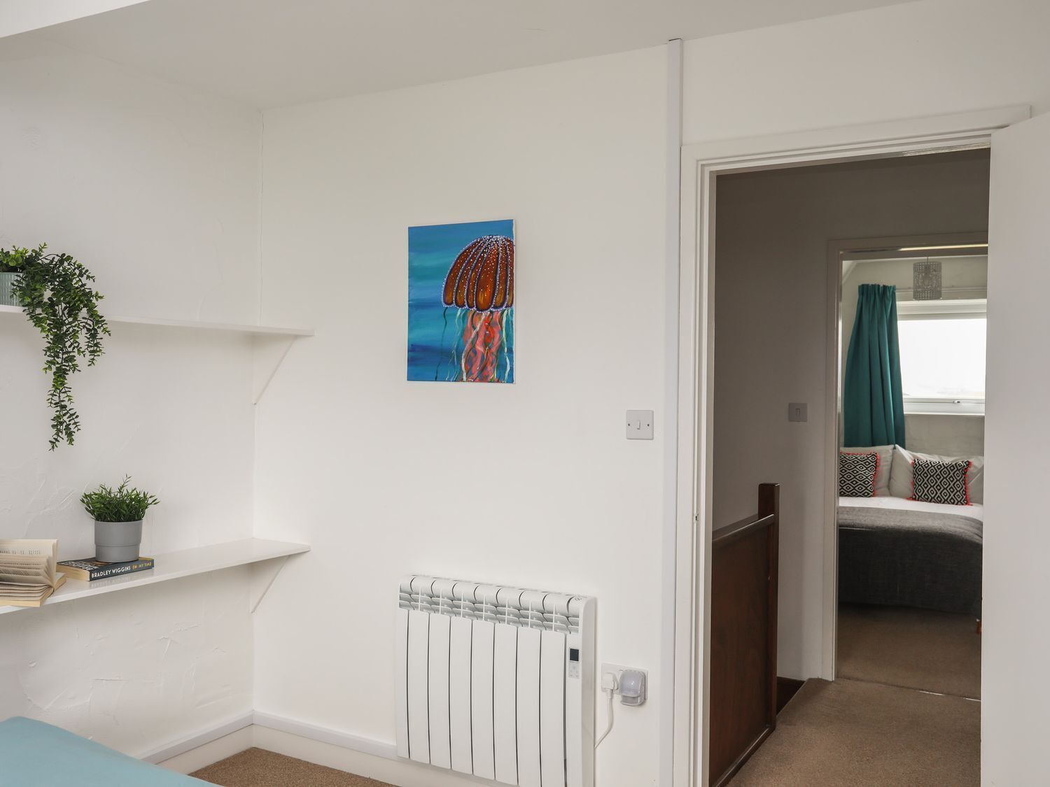 A room with a radiator, a shelf with books and a plant, and a painting of a jellyfish on the wall.