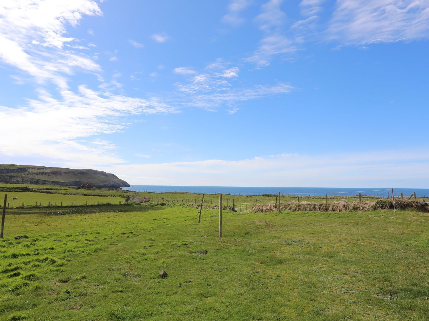 A coastal landscape with a grassy field, a wooden fence, and a distant view of the sea.