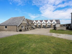 A row of single-story buildings with a flat roof, a central courtyard with picnic tables, and a grassy area in front. - Penrhyn - 4 Ty'n Don (Pwllheli)