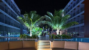 A nighttime outdoor area with a circular seating area, palm trees, and a pool. - PORTO ALTO RESORT (Ipojuca)