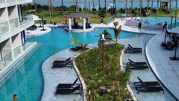 A resort pool area with a curved design, palm trees, and a view of the ocean. - PORTO ALTO RESORT (Ipojuca)