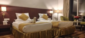 A hotel room with two beds, a green armchair, a small table with a vase of flowers, and a window with curtains. - Cityhouse - Abora (Kasaya)