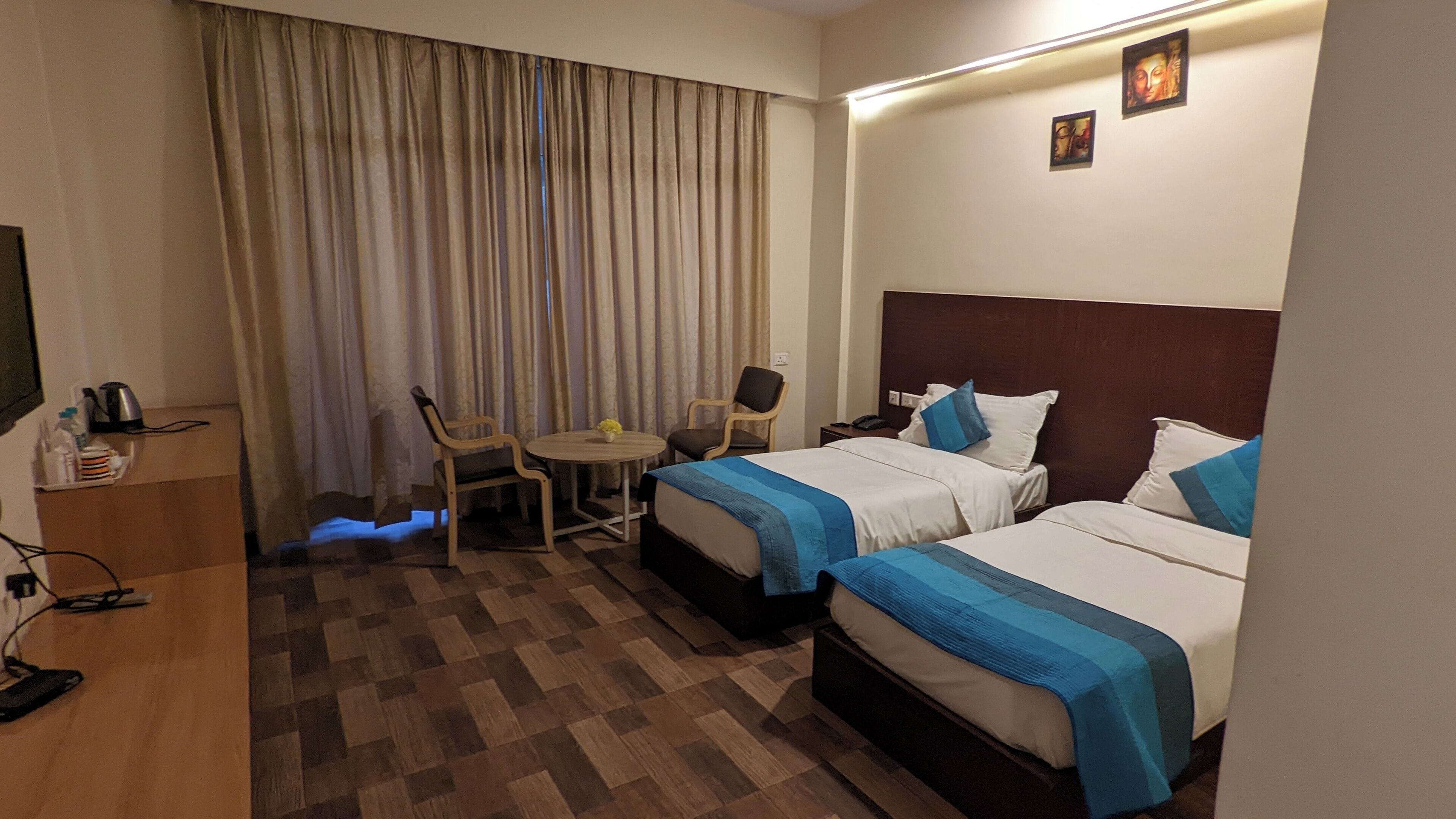 A hotel room with two beds, a desk, a chair, a small table with a vase, and a TV on a wooden cabinet.