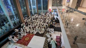 A large group of people seated on a carpeted floor in a spacious indoor area with high ceilings and large windows. - Cityhouse - Abora (Kasaya)