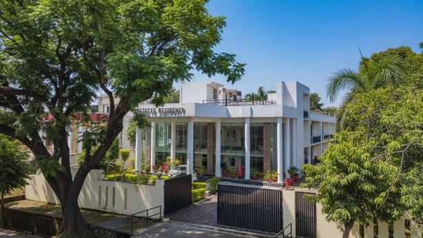 A modern building with a sign reading "RESIDENCY." It features a central courtyard with a fountain, surrounded by trees and potted plants. - Cityhouse - Abora (Kasaya)