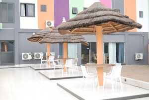 Un espacio al aire libre techado con mesas y sillas, unidades de aire acondicionado y un edificio de paredes coloridas.