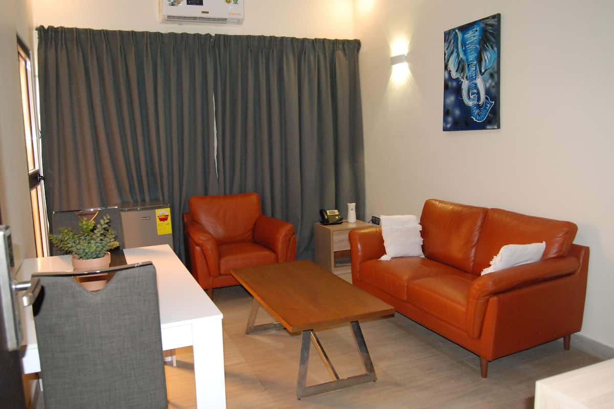 A living room with a white table, two orange leather sofas, a grey armchair, a wooden coffee table, a small side table with a plant, and a painting on the wall.