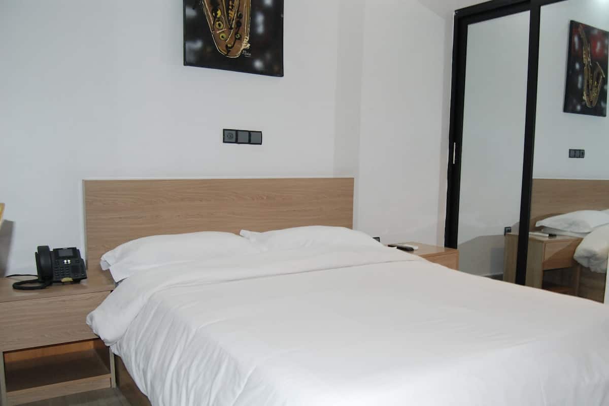 A hotel room with a bed, a bedside table with a phone, and a mirror reflecting the room.