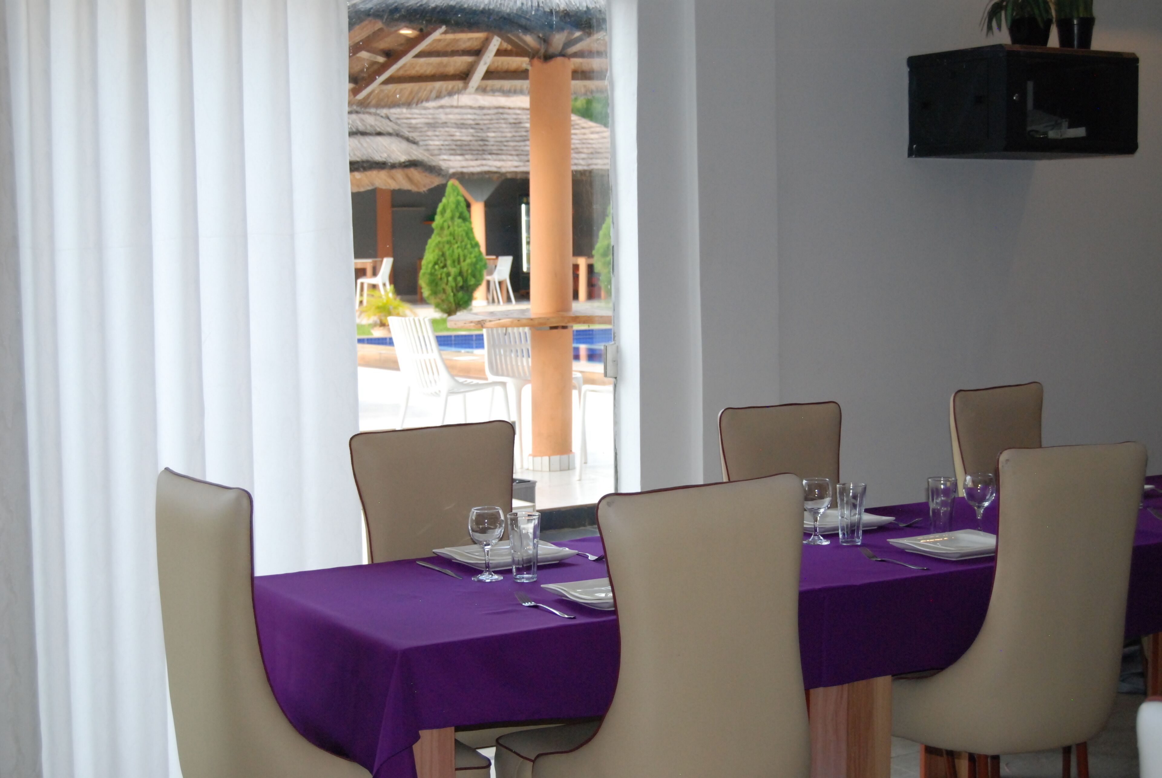 A dining area with a purple tablecloth, white chairs, and a view of an outdoor patio with umbrellas and chairs.
