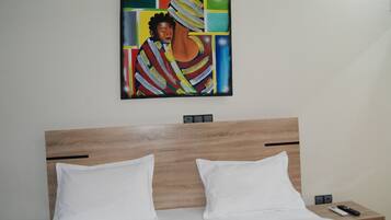 Habitación de hotel con cabecera de madera, dos almohadas blancas, una cama, una mesita de noche con un control remoto y un cuadro en la pared.