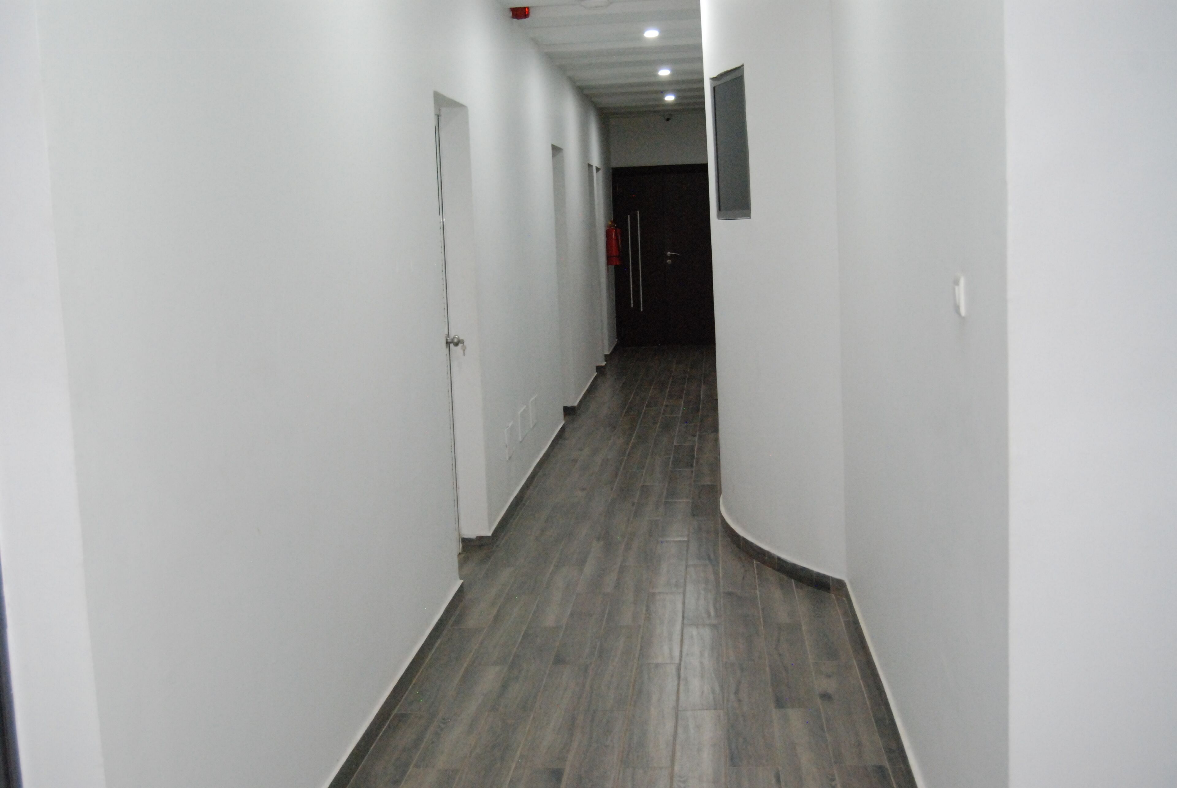 A narrow, well-lit hallway with white walls and dark wooden flooring.