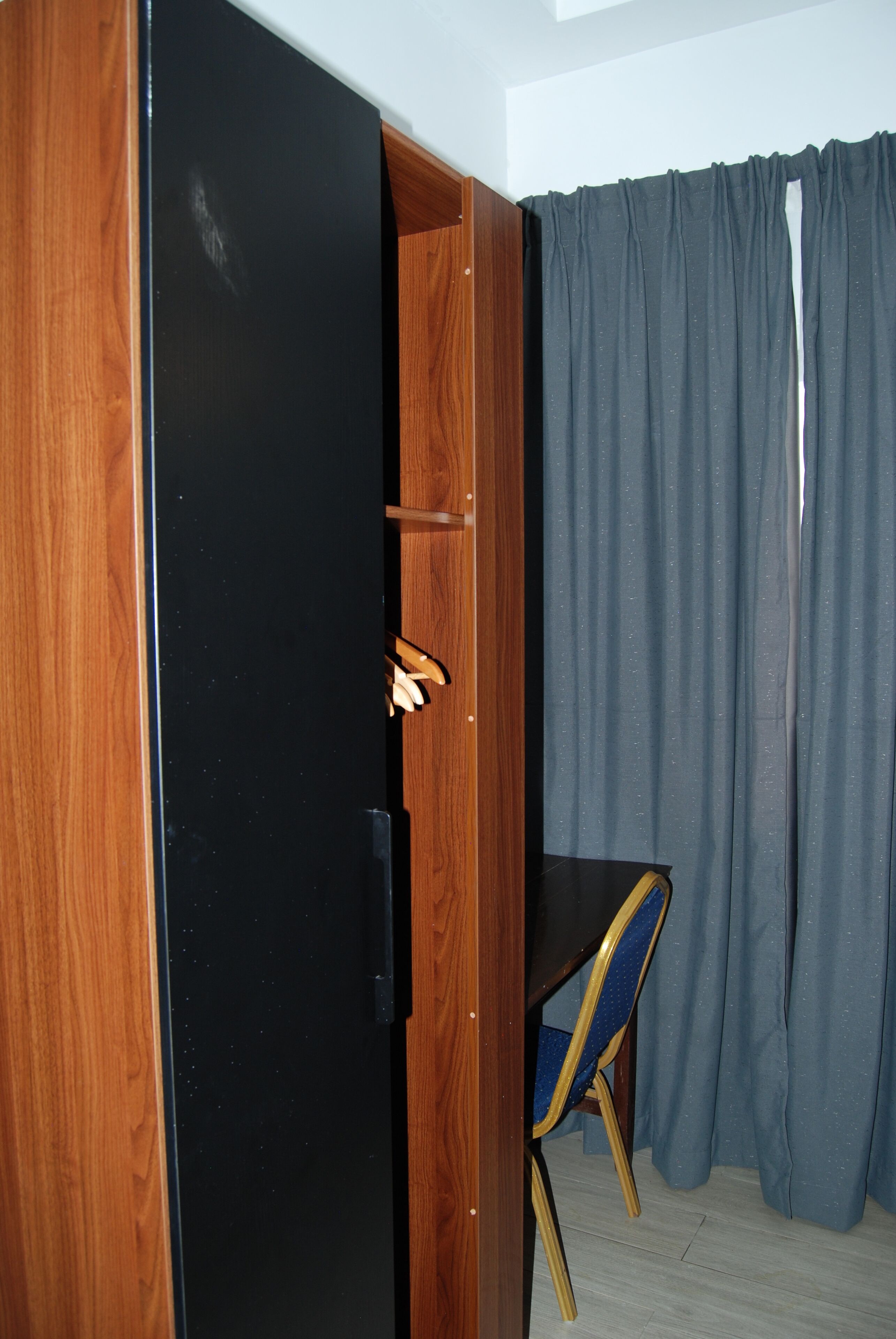 A room with a wooden wardrobe, a blue chair, and grey curtains.
