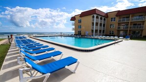 A poolside area with blue lounge chairs, a swimming pool, and a building with balconies. - Point East 320 (New Smyrna Beach)