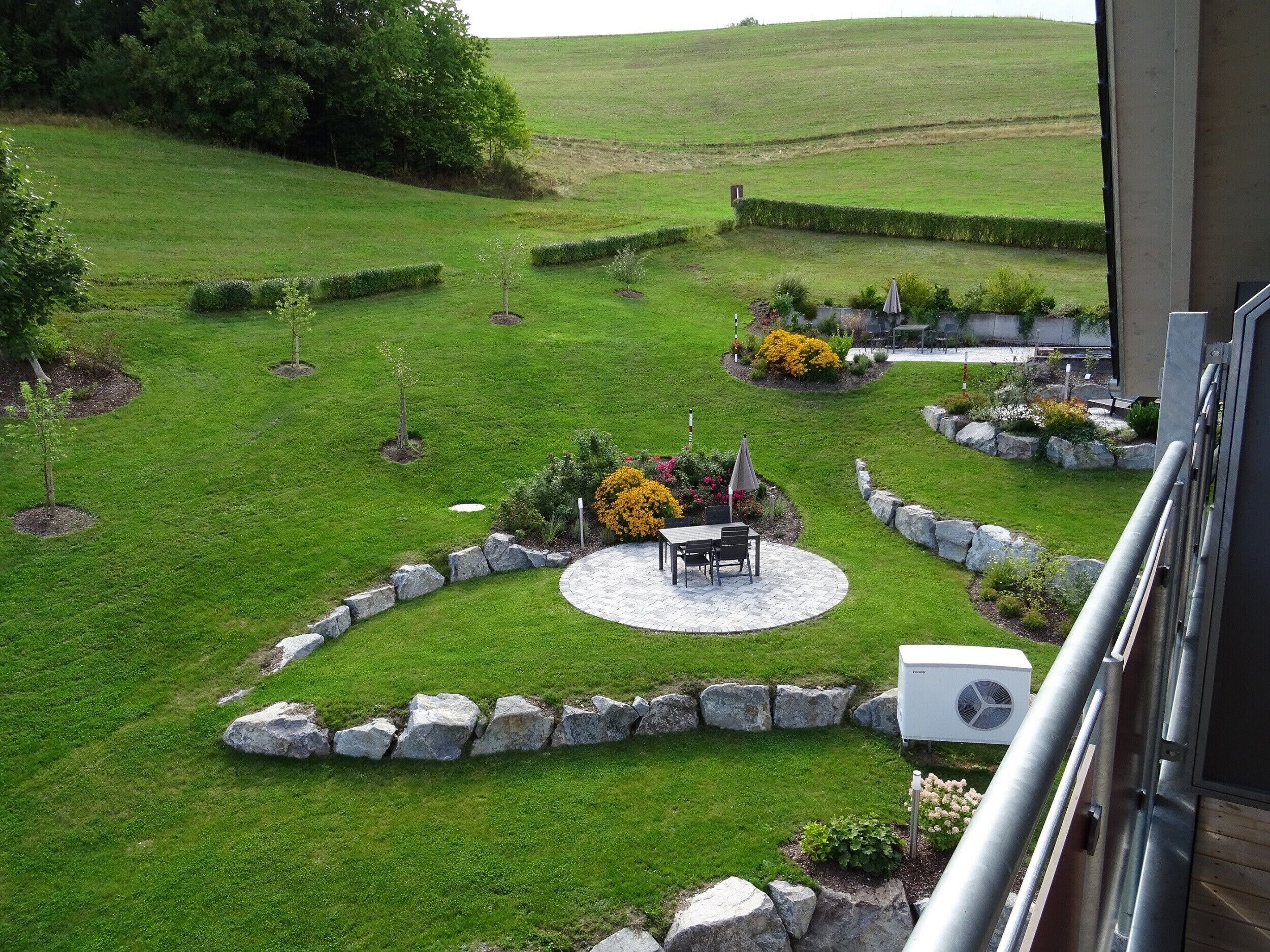 Un jardín bien cuidado con un área de patio, bordes de piedra y diversas plantas.