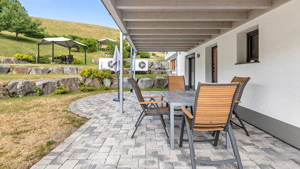 An outdoor patio with a table and chairs, a covered area, and a view of a hillside. - Apartment 'Holzwieb' with Private Terrace, Shared Garden and Wi-Fi (Unterkirnach)