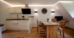 Una cucina moderna con mobili bianchi, un tavolo da pranzo in legno e una TV a parete.