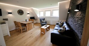 Un salon moderne avec un canapé en cuir noir, une table à manger en bois et un mur décoratif en pierre.