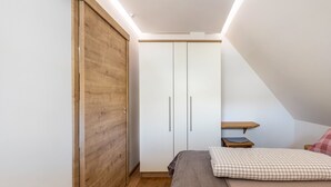 A bedroom with a wooden wardrobe, a bed with a checkered pillow, and a small wooden table.