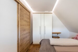 Ein Schlafzimmer mit einem Holzkleiderschrank, einem Bett mit einem karierten Kopfkissen und einem kleinen Holztisch.