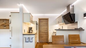 A compact kitchen with a coffee machine, wooden cabinets, and a dining area with a table and chairs.