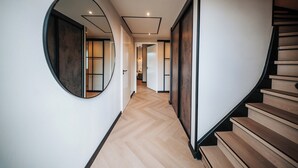 A modern hallway with a wooden staircase, a round mirror, and a herringbone floor. - Beautiful Holiday Home in Waarland (Waarland)