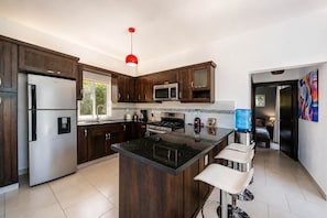 Cocina moderna con armarios de madera oscura, electrodomésticos de acero inoxidable, una isla central y una lámpara colgante roja.