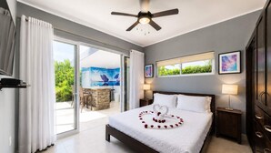 A hotel room with a bed, a ceiling fan, a view of greenery, a dining area, and artwork on the walls. - Sunlit Pool Hideaway ● 2 En-Suite Kings (Sosúa)