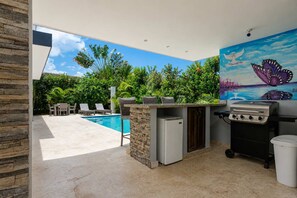 An outdoor kitchen area with a pool, lounge chairs, and a mural.