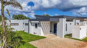 Uma casa moderna de dois andares, com telhado plano, entrada central e pequena varanda.