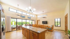 A spacious kitchen with a large island, wooden cabinets, and a dining area with a TV. - Modern 3BR Villa · Private Pool · Casa Linda Sosúa (Sosúa)