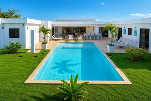 A modern pool house with a rectangular pool, surrounded by a well-maintained lawn and potted plants. - Luxury Getaway • gate comunity (Sosúa)