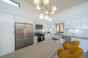 A modern kitchen with a central island, stainless steel appliances, and a yellow chair. - Luxury Getaway • gate comunity (Sosúa)