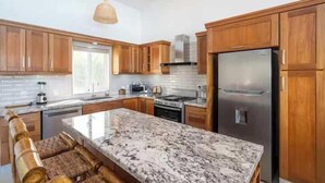 A modern kitchen with wooden cabinets, a granite countertop, stainless steel appliances, and a built-in oven. - Luxurious 4-bedroom villa in Casa Linda. (Sosúa)