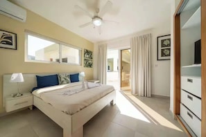 Une chambre à coucher comprenant un lit, une table de chevet, un ventilateur de plafond, une fenêtre et une porte donnant sur un balcon.