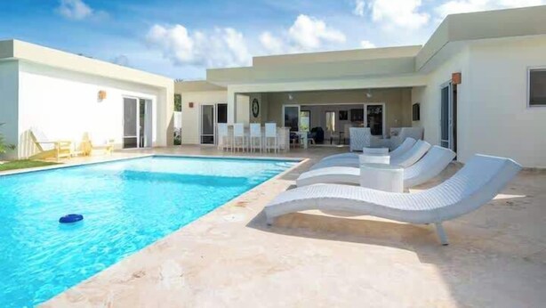 A modern pool area with lounge chairs, a clear blue pool, and a covered patio. - Luxurious 4-bedroom villa in Casa Linda. (Sosúa)