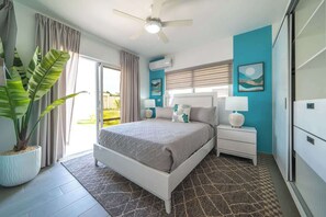 Un dormitorio con cama, mesitas de noche, ventilador de techo, ventana con cortinas, planta en maceta y aire acondicionado de pared.
