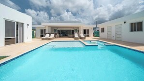 A modern pool area with clear blue water, a covered seating area, and a white building with large windows and doors. - Private Pool • Luxury • Casa Linda (Sosúa)