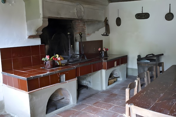 Une cuisine avec un mur recouvert de carreaux, un four en briques et une longue table en bois.