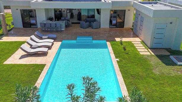 A modern house with a swimming pool, outdoor seating, and a well-maintained lawn.