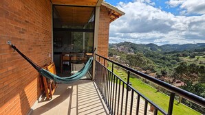 Un balcón con hamaca, paredes de ladrillo y vistas a un paisaje verde.