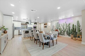 A modern kitchen with white cabinets, a dining area with a table set for four, and a cactus-themed wall mural. - 4BR En-Suite | Walk to Old Town | Pool-Spa-Sauna (Scottsdale)