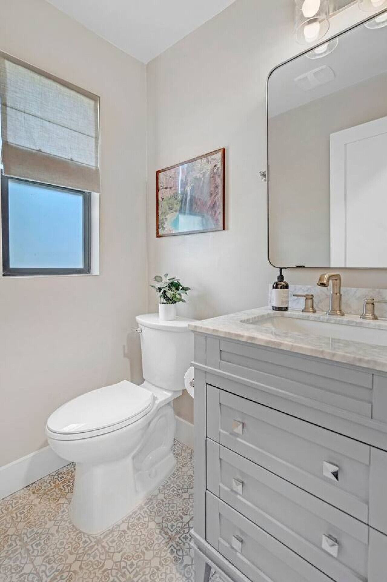 A bathroom with a toilet, a sink with a mirror, and a window.
