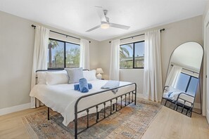 Une chambre à coucher avec un lit, un ventilateur de plafond, une grande fenêtre et un miroir.