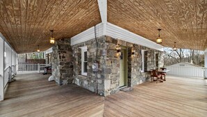 Un espacio al aire libre cubierto con una pared de piedra, suelo de madera y un área de estar con mesas y sillas.